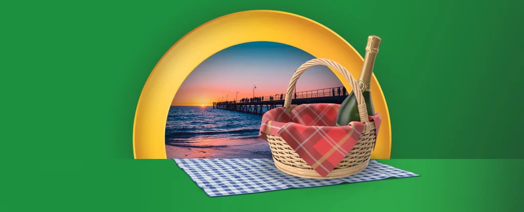 A picnic blanket and basket containing a bottle of fizz features. In the distance is an Adelaide beach. On a green background.