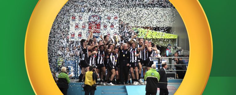 An AFL team celebrates winning the AFL Grand Final with the trophy on a podium. On a green background.